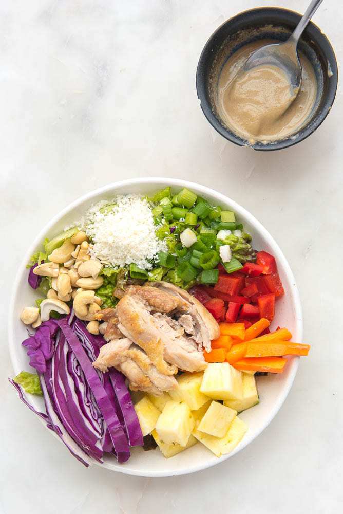 Colorful Asian salad on a plate with a side bowl of dressing