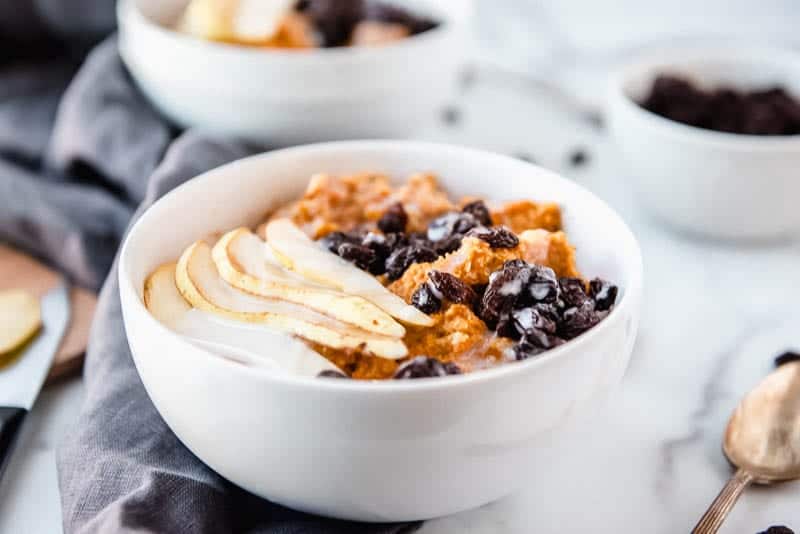 a horizontal closeup of the aip breakfast porridge in a while bowl, topped with fresh sliced pears, raisins, and drizzled with melted coconut butter