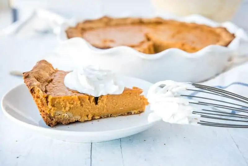 a slice of Paleo sweet potato pie on a plate with a dollop of coconut whipped cream. The rest of the pie is in the background