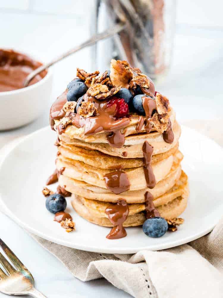 stack of AIP Cassava flour pancakes covered with chocolate sauce, granola and berries