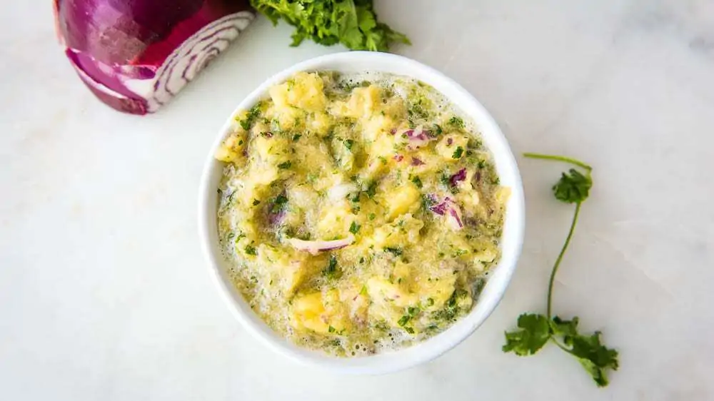 Pineapple Salsa in a bowl surrounded by cilantro and red onion