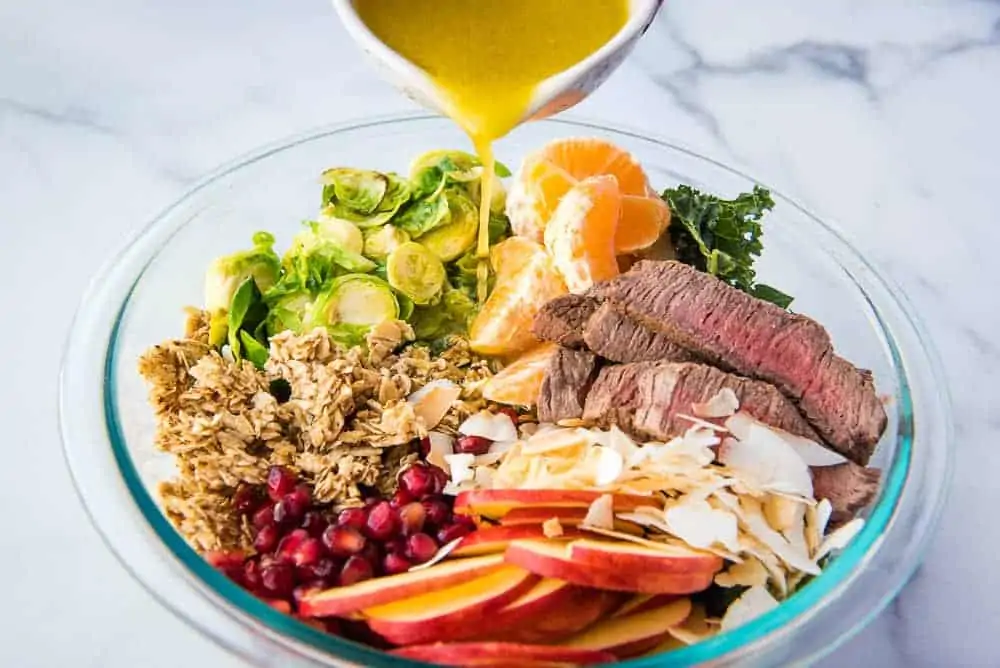 Winter steak salad cooked ingredients in a bowl with the dressing being poured on top