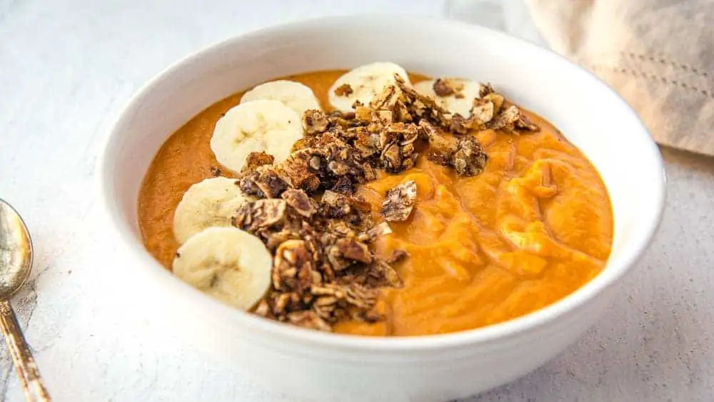 Sweet Potato Breakfast Bowl from the side, covered with fresh banana slices and tigernut granola