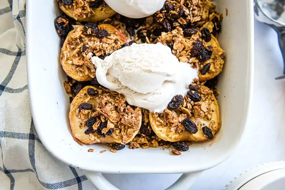 baked apples in a white baking dish topped with vanilla ice cream