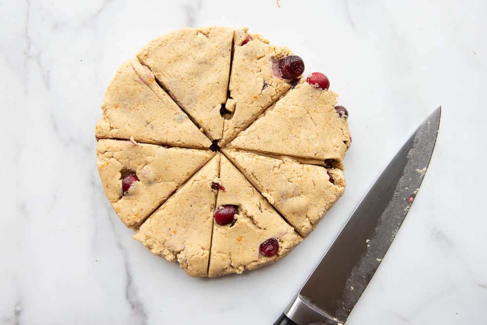 the dough of the cranberry orange scones on a counter cut into 8 pieces, with a knife laying beside it