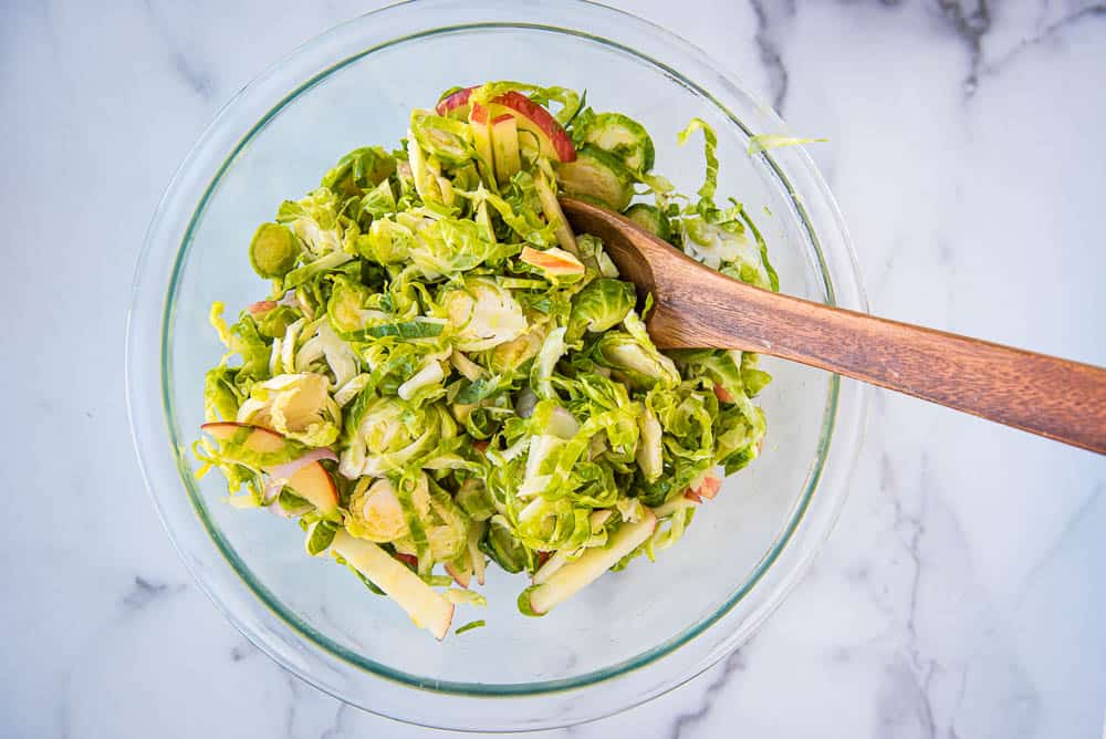 An overhead view of brussles sprouts slaw in a glass bowl with a wooden spoon.