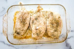 An overead view of baked chicken breasts seasoned in a glass baking dish.