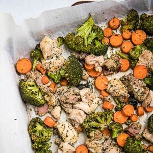 Extreme close-up high angle view of sheet pan corner with roasted chicken, broccoli and carrots.