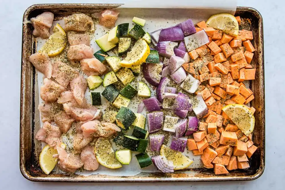 sheet pan with chicken, zucchini, red onions, sweet potatoes and lemons covered with greek seasoning mix