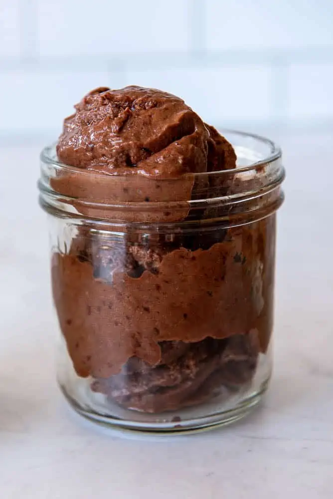 A side view of a single portion sized mason jar containing three scoops of dark brown AIP Cherry Chocolate Ice Cream.