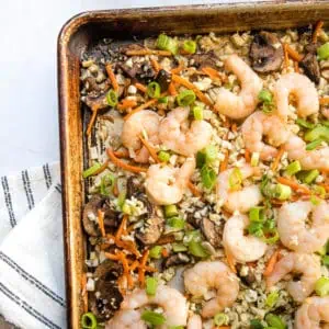Overhead view of top left corner of sheet pan with vegetables and shrimp